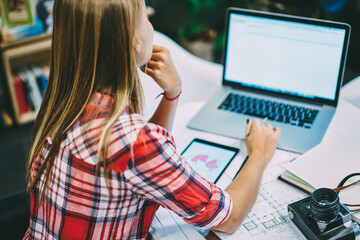 Back view of student in casual wear sitting at modern laptop and preparing for studying seminar in...