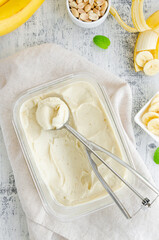 Homemade banana ice cream in a glass container with a spoon for ice cream on a wooden background. Healthy dessert. Vertical, top view, copy space.