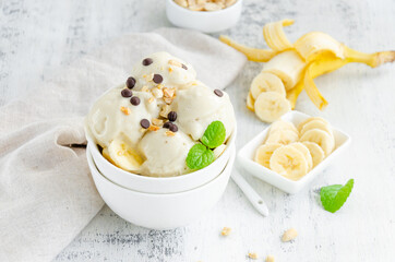 Homemade vegan banana ice cream in a bowl with peanuts and chocolate on a wooden background. Healthy dessert. Horizontal, copy space.