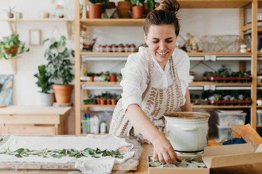 Smiling woman in light clothes and in an apron creates a pattern on a white t-shirt