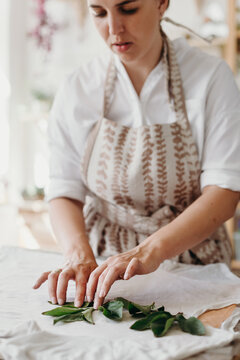 Female florist or decorator puts leafes on a white cloth. Creating process.