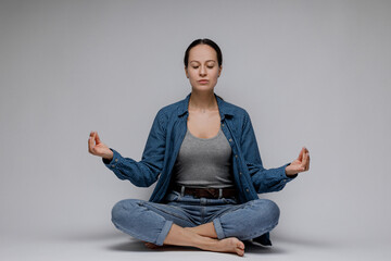 Young woman looks up in casual clothes and meditates while sitting on the floor on a light background. Relaxation.