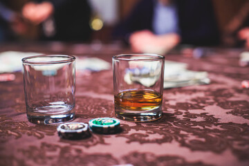 View of poker table with pack of cards, tokens, alcohol drinks, dollar money and group of gambling rich wealthy people playing poker