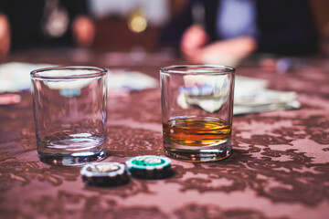 View of poker table with pack of cards, tokens, alcohol drinks, dollar money and group of gambling rich wealthy people playing poker