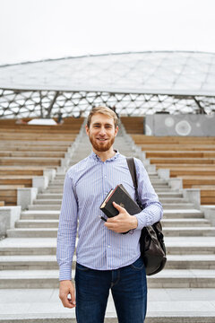 Bearded male standing with book by stairs