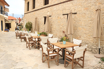 Fototapeta na wymiar Greek ancient summer cafe beige in the street. Wooden chairs, tables, umbrellas.