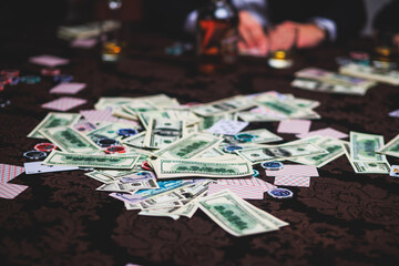 View of poker table with pack of cards, tokens, alcohol drinks, dollar money and group of gambling rich wealthy people playing poker