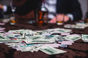 View of poker table with pack of cards, tokens, alcohol drinks, dollar money and group of gambling...