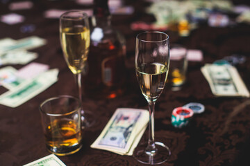 View of poker table with pack of cards, tokens, alcohol drinks, dollar money and group of gambling rich wealthy people playing poker