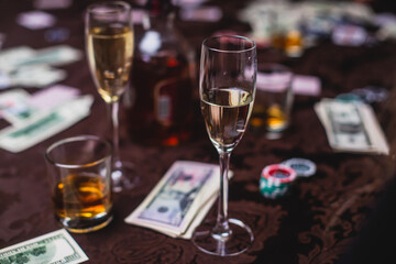 View of poker table with pack of cards, tokens, alcohol drinks, dollar money and group of gambling rich wealthy people playing poker