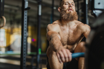 Strong and healthy man working out on a rowing machine, inside a crossfit gym.