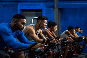 Group of sporty people training on exercise bikes together at gym.