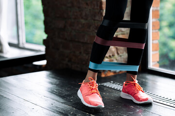 Close-up of the legs of a girl in pink sneakers taking steps with three different elastic expanders at the ankles, calves and knees in the gym.