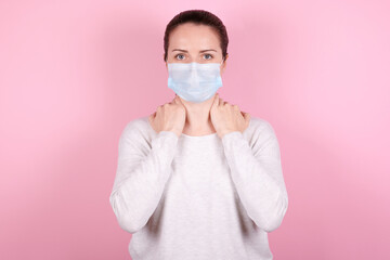 Portrait of a brunette girl in a medical mask. Isolated on pink background.