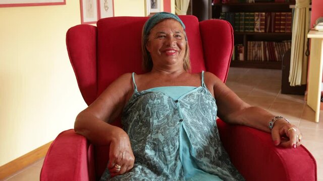 Video in 4k di Signora anziana sorridente che si rilassa nella poltrona rossa mentre guarda divertita la tv
