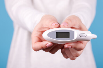 Electronic thermometer in hands on a blue background. Close up photo.
