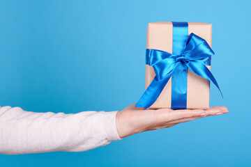Present box with blue ribbon in hand on blue background.