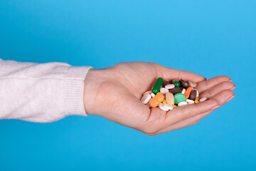 Different pills and drugs in hand on blue background.