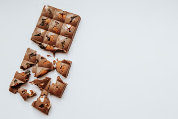 Close up picture of chocolate bar broken on small pieces with some nuts located on light background. Copy space concept with unhealthy sweets. Flat lay composition with candy on side.