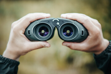 Close-up of a hunter man's hands holding binoculars on the blurred background.