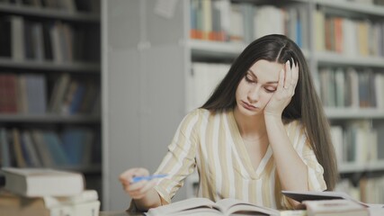 Tired young woman is preparing for examination at university library