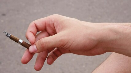 a man flicks ash from a cigarette while on the street.