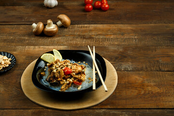 A plate of funchoses with chicken and vegetables in pad Thai sauce sticks on a stand next to vegetables.
