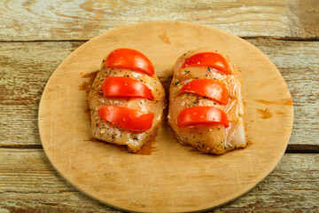 Marinade chicken breast stuffed with tomatoes on a round wooden board.