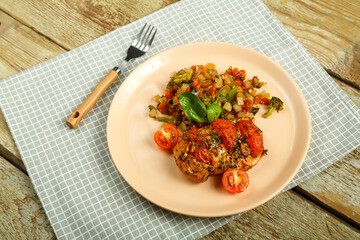 Baked chicken breast with tomatoes and vegetables garnished on a plate with fork on a linen napkin.