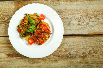 Baked chicken with tomatoes in spices with a side dish of frozen boiled vegetables on a white plate. Copy space.