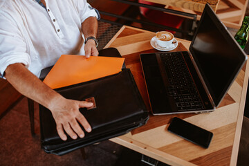 Closeup of a hands of a businessman working on a laptop, drinking coffee and putting business documents in a bag