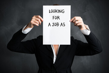 businesswoman holding a sign with the message LOOKING FOR A JOB AS in front of a chalkboard