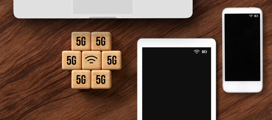 cubes with 5G and WLAN symbol besides tablet, smartphone, and laptop on wooden background