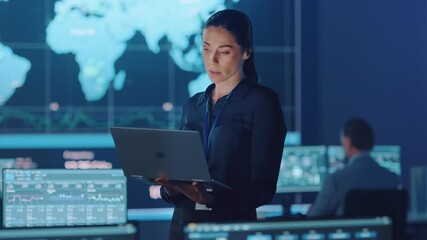 Female Project Leader is Standing with Laptop Computer and Checking Work Data. Science Engineers Work Around Her. Telecommunications Control Monitoring Room with Neural Network on Servers.