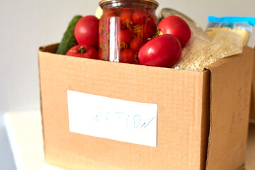Box for a charity donation with food. Canned food, pasta, pickled tomatoes, vegetable, rice. Food delivery or food donation concept.