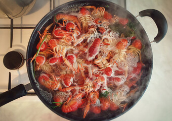 Cooking river crayfish, or crawfish, at home on a traditional recipe. A lot of red, freshwater lobsters boiling in a big bowl on hob. Preparing delicious, non gmo, organic food in house conditions.