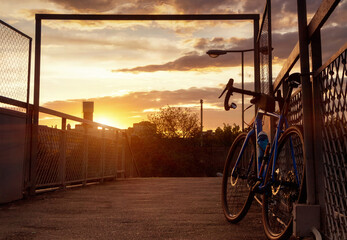 A road bike is parked near the fence. Bicycle silhouette on sky background at sunset.
