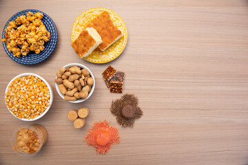 Top view of typical June Party foods on a wooden table: Popcorn, cornmeal cake, corn kernels, peanut pods, peanuts candies (paçoca) and dulce de leche. Small country hats. Copy space. Selective focus.