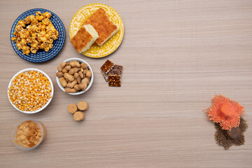 Top view of typical June Party foods on a wooden table: Popcorn, cornmeal cake, corn kernels, peanut pods, peanuts candies (paçoca) and dulce de leche. Small country hats. Copy space. Selective focus.