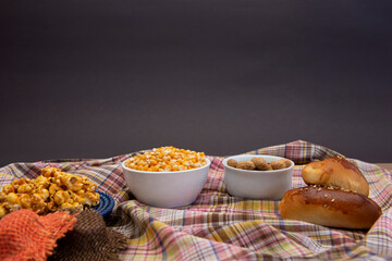 Close up of typical June Party foods on a wooden table: Popcorn, cornmeal cake, corn kernels, peanut pods and small country hats. Copy space. Selective focus.