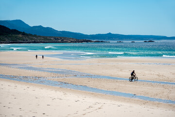 seascape of a beach in the atlantic ocean with fine sand and small silhouettes of people walking and cycling