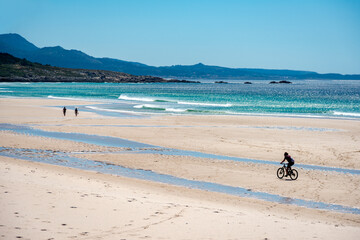 seascape of a beach in the atlantic ocean with fine sand and small silhouettes of people walking and cycling