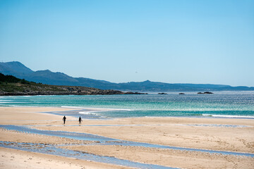 seascape of a beach in the atlantic ocean with fine sand and small silhouettes of people walking