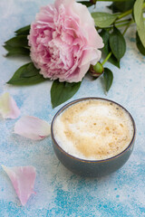Morning cup of coffee or cappuccino and pink peonies on blue concrete table. Creative breakfast for Woman or Mother day.