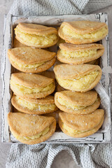 Homemade buns or pastries with cottage cheese on a wooden tray, light grey stone background. Traditional Russian pastry Sochnik. Selective focus. Top view.