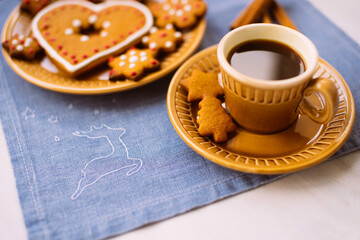 A cup of coffee and a delicious Christmas cookie lies on a blue linen napkin on a white table.