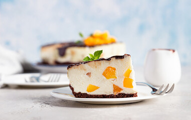 Piece of no bake apricot cheesecake garnish with chocolate glaze, fresh apricots and mint, light stone background. Delicious summer dessert.