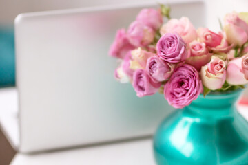 Vase with roses on the table, in the background a laptop on a blurred background.