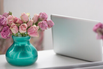 Workplace in the office, on the table a vase of flowers and an open laptop.