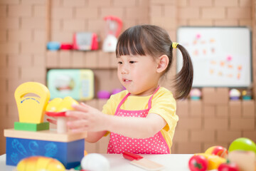 toddler girl pretend play food preparing role against cardboard blocks kitchen background